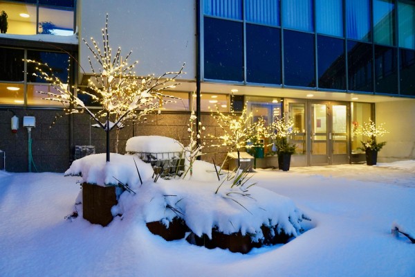Kommungårdens innergård och huvudentré är täckta av snö. Julbelysningen lyser upp.