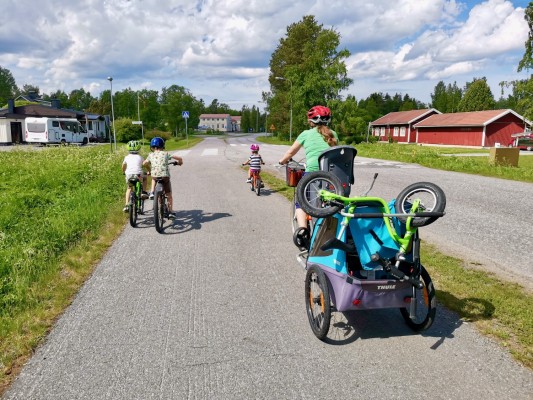 Aikuinen ja kolme lasta pyöräilevät pyörätiellä Pännäisissä. Aikuisella pyöräilijällä on polkupyörävaunu takanaan.