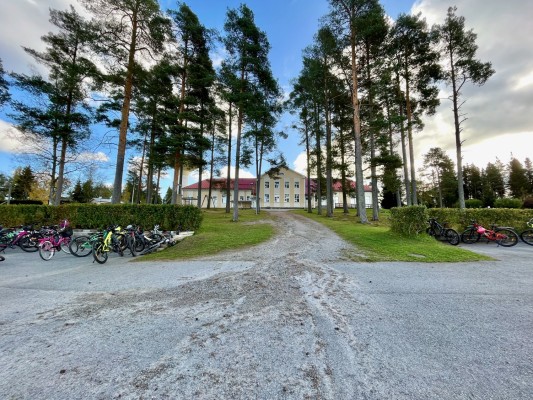 Taustalla kukkulalla näkyy Kållby skola. Se on keltainen puurakennus. Kuvan etuosassa paljon lasten pyöriä.
