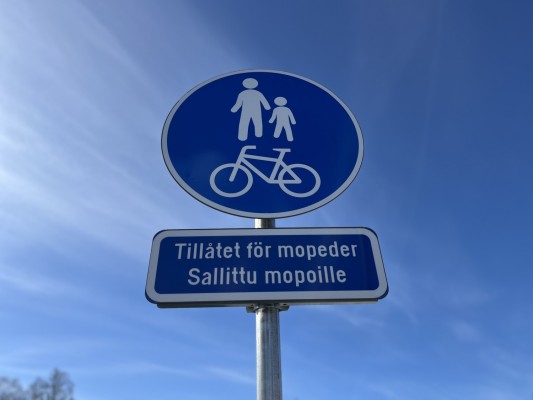 Ett runt trafikmärke för gång- och cykelväg. Tilläggstext: Tillåtet för mopeder.