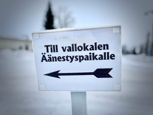 Kyltti, jossa lukee "Till vallokalen" ruotsiksi (suom. Vaalihuoneistolle") ja nuoli vasemmalle.