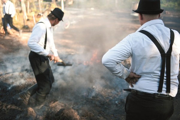 Två män vaktar en brinnande tjärdal.
