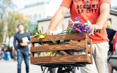 Polkupyöräkori lähikuvassa. Korissa on juureksia, vihanneksia ja kukkia.