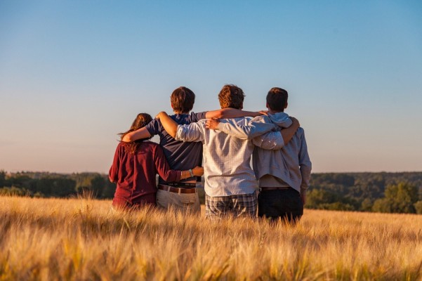 Fyra ungdomar står på ett sädesfält med armarna om varandras axlar.