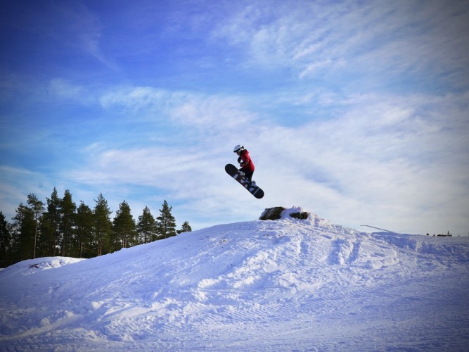 En ung person hoppar med snowboard över ett gupp i Bergöbacken.