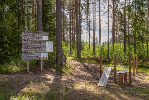 Startplatsen vid Vildmarkscentret i Lappfors. Skylt som visar avstånd till olika deletappen. Träd och ett litet utegym
