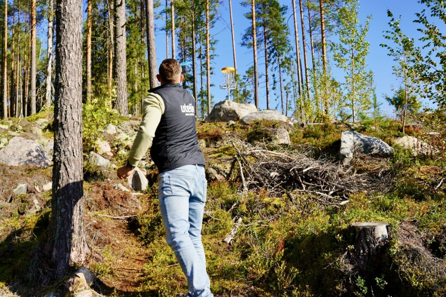 En man kastar frisbee mot en korg upp på en backe.