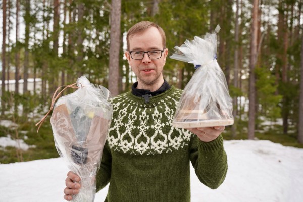 Mattias Kanckos står ute framför några träd, håller Pedersöreklockan och blommor i händerna.