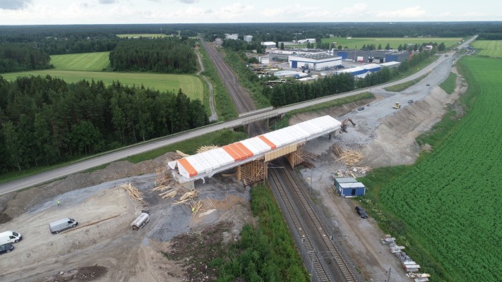 En flygbild över den nya järnvägsbron i Kållby. Den nya bron är ännu täckt med skyddsplats. Man ser också järnvägen under bron och omgivande miljö.