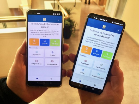 Två mobiltelefoner med Pedersöre-appen i rutan. Både den svenskspråkiga och den finskspråkiga versionen.