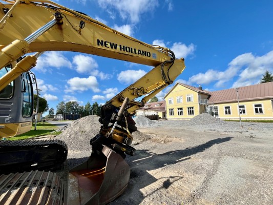 Östensö skola i bakgrunden. Närmast kameran en grävmaskin. Det är grushopar på gården.