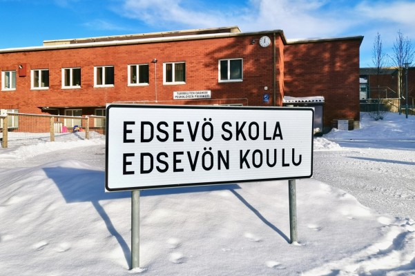 En vinterbild av Edsevö skola. Tegelbyggnad. Framför den en skylt med texten Edsevö skola, Edsevön koulu.