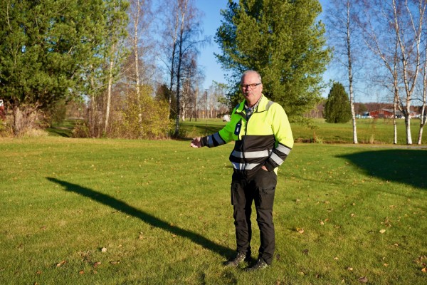 Kommunens trädgårdsmästare Hans Björklund står på en gräsmatta och pekar mot området bakom sig.