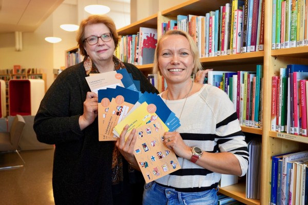 Bibliotekschefen Solveig och specialbibliotekarien Lisa står mellan bokhyllor och håller i läskampanjens poängkort.