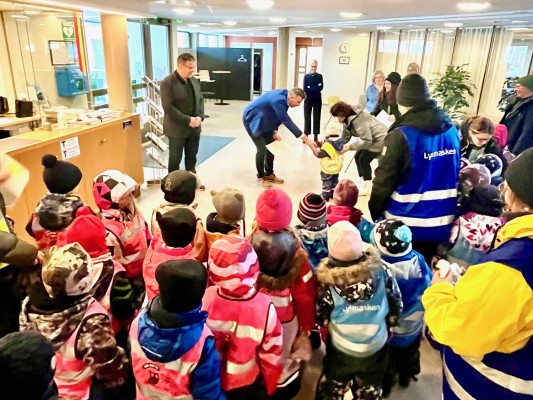 Kommundirektören och kommunfullmäktiges ordförande tar emot ett dokument av dagisbarn från Dressinen i kommungårdens entréhall.