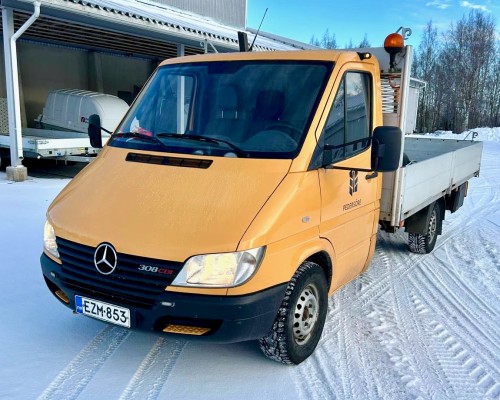 Keltainen lava-auto on pysäköity lumiselle maalle konevarikon pihalla.