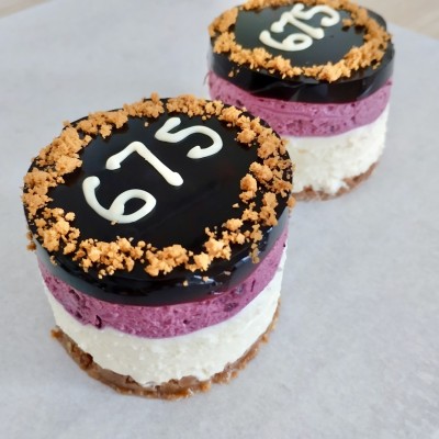 En blåbärscheesecake med tre fyllningar, siffrorna 675 skrivet på toppen.