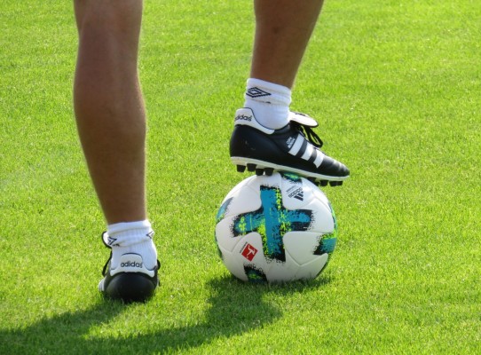 Närbild av en fotbollsspelare som har ena foten på en fotboll.