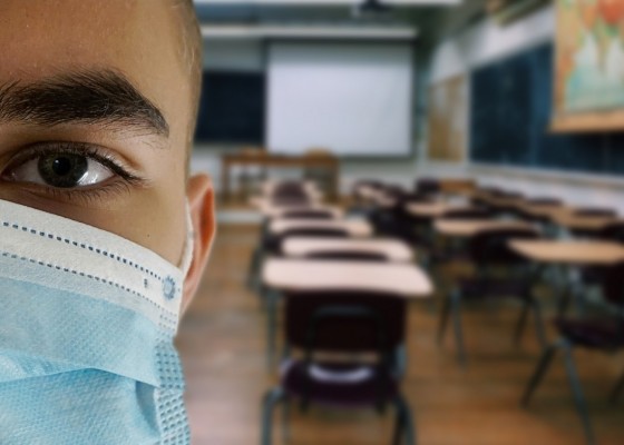 Närbild av person med munskydd i ett klassrum.