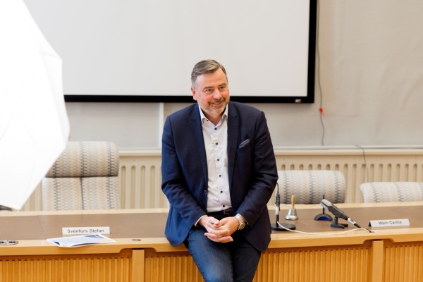 Stefan Svenfors halvsitter på ett bord i fullmäktigesalen.