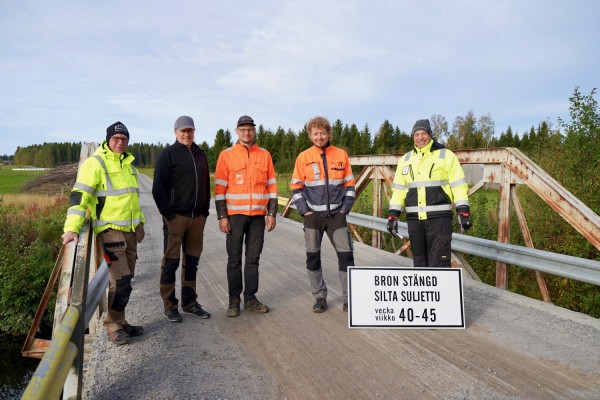 Fyra entreprenörer och kommunens vägmästare står på Kittholmsbron som ska renoveras. En skylt berättar att bron är avstängd veckorna 40-45.
