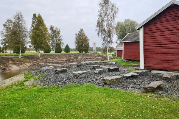 Delar av en damm, spår av grävmaskinens arbete på marken och två bodar. Ankdammen-området i Bennäs.