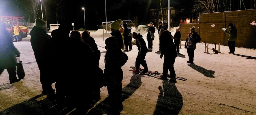 Det är mörkt. En samling människor står på skolgården som är upplyst.