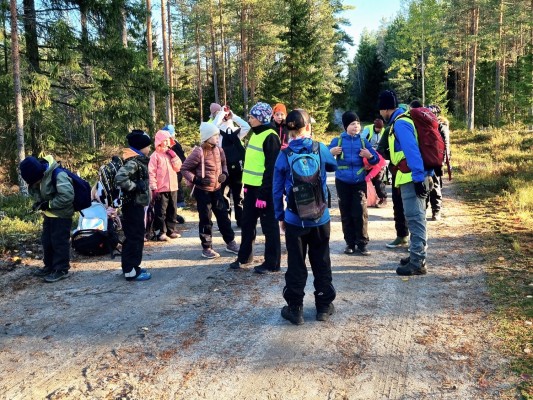 En stor grupp elever har samlats på en grusväg. Solen skiner, de står och vilar.