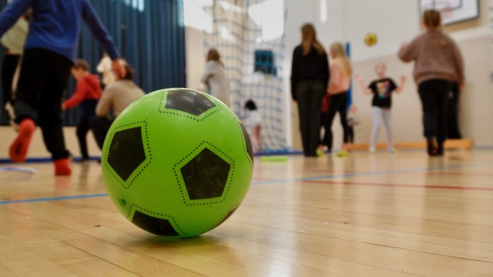 En plastfotboll på ett gymnastiksalsgolv. I bakgrunden syns människor.