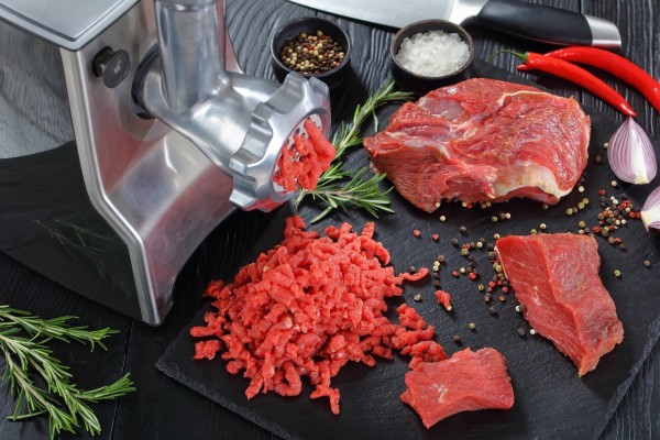 En köttkvarn och köttbitar och lite köttfärs på ett bord.