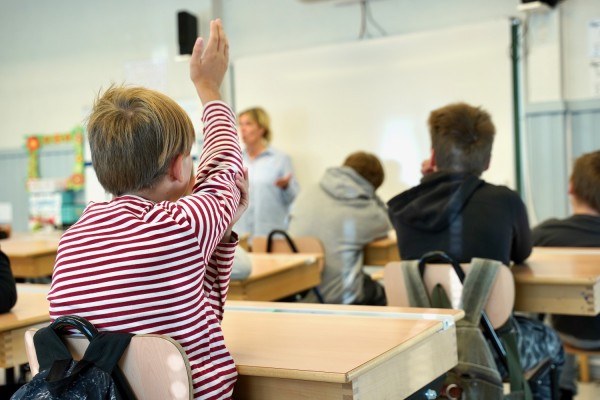 En elev håller upp sin hand i luften (markerar) i ett klassrum.
