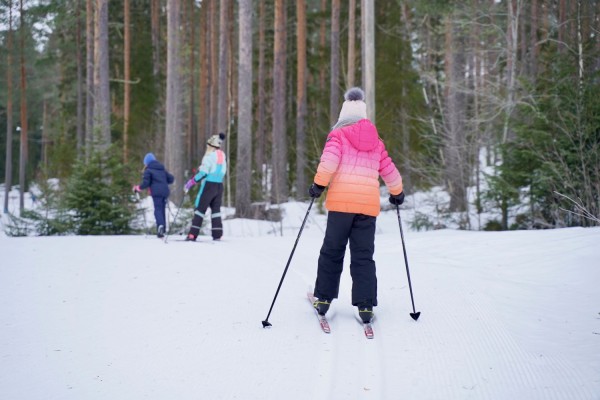 Några flickor åker skidor på ett spår i skogen.