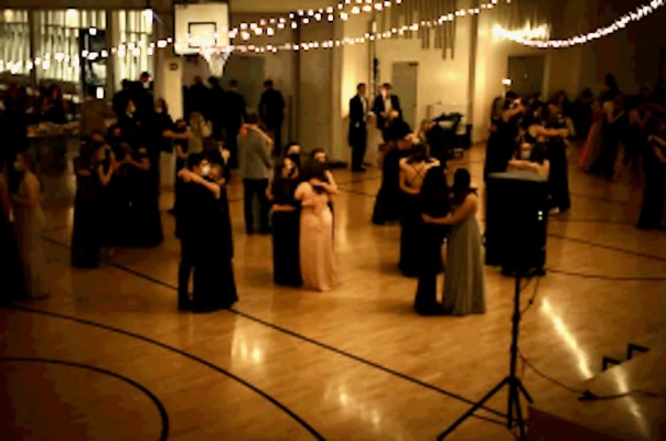 En festlokal med dämpat ljus. Det dansar flera par på golvet.